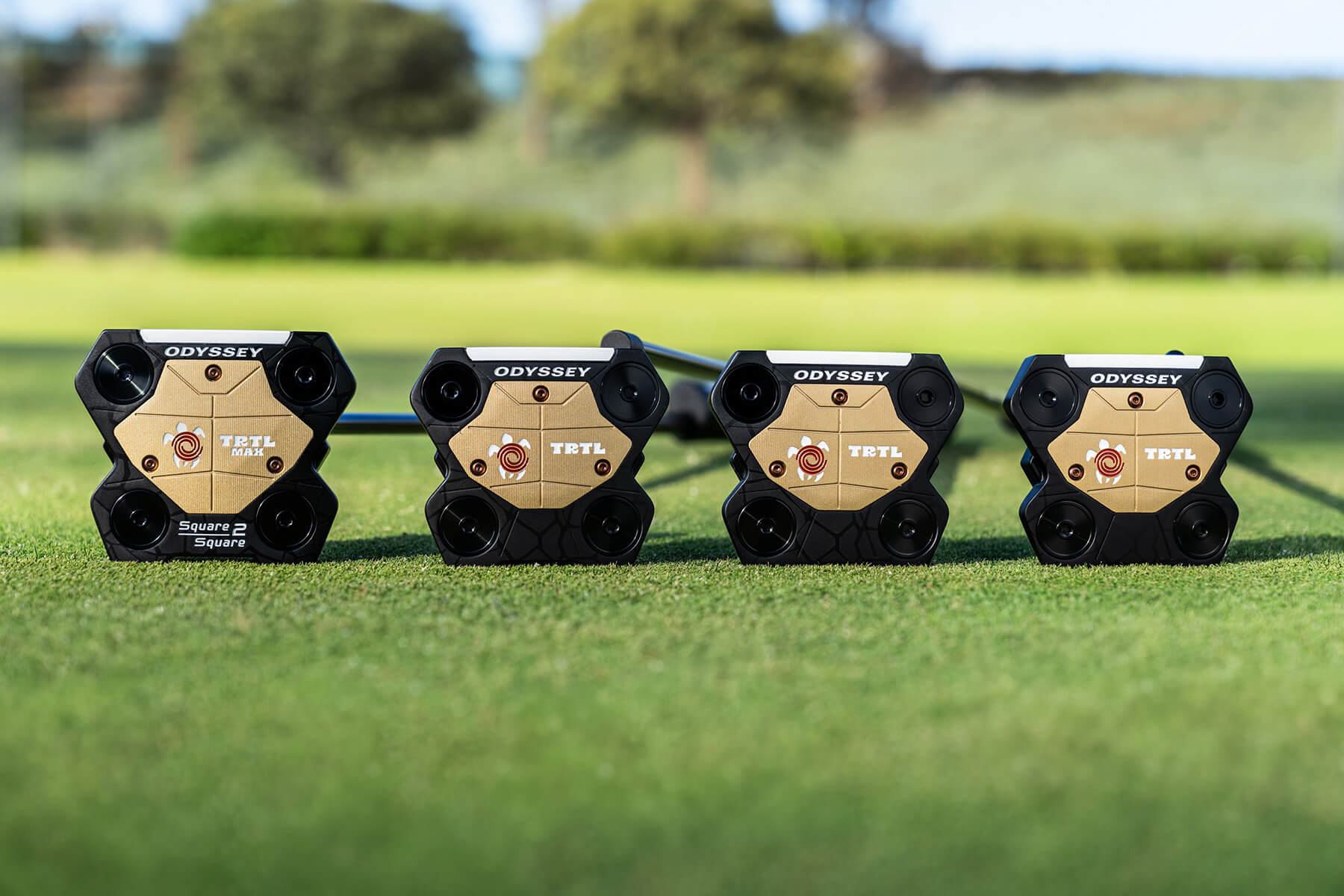 The soles of all four TRTL putters lined up on the grass
